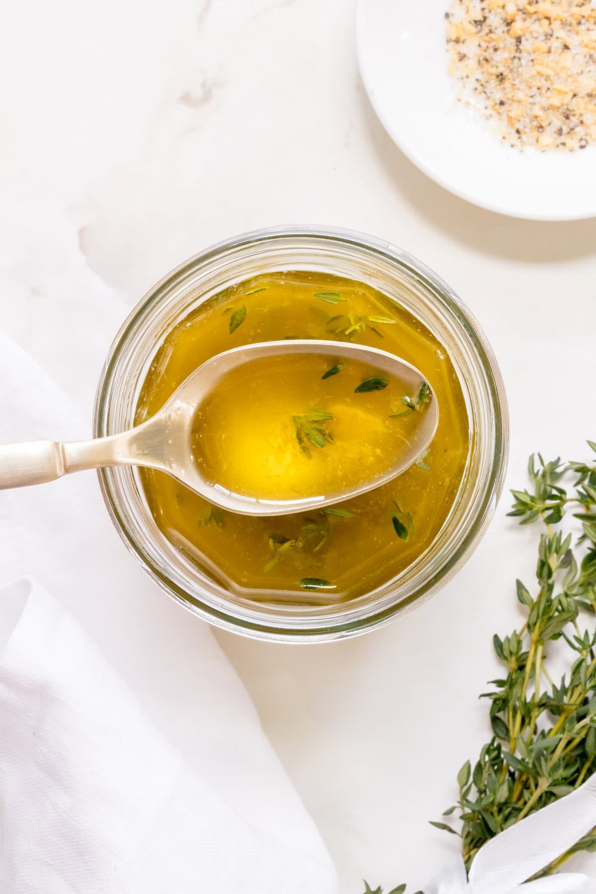 a glass jar of apple cider vinaigrette with a gold spoon and bunch of thyme.