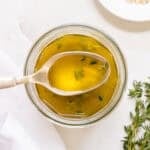 apple cider vinaigrette in a glass jar with a scoop pulled out on a gold spoon.