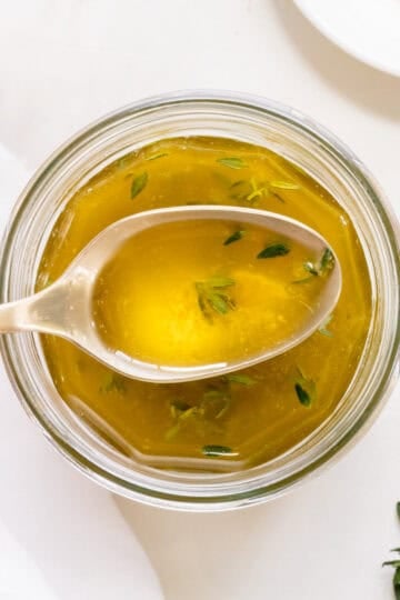 apple cider vinaigrette in a glass jar with a scoop pulled out on a gold spoon.