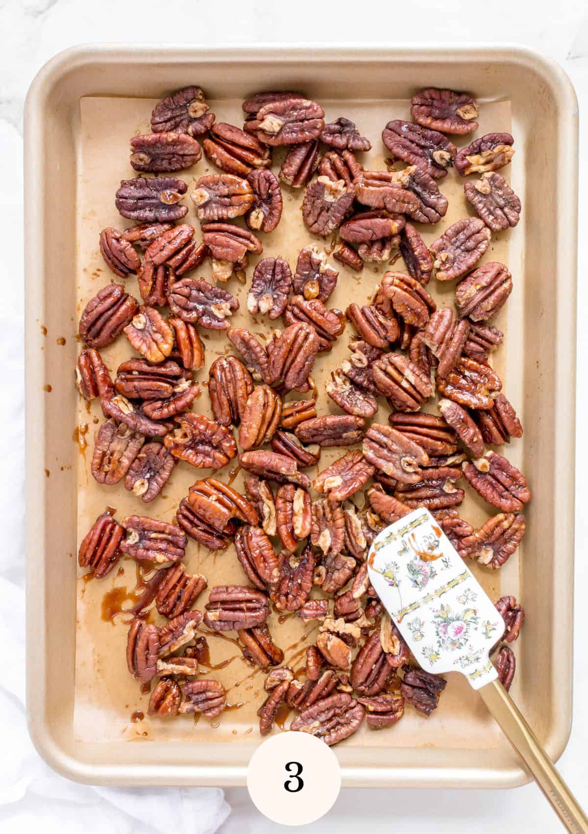 gold sheet pan of roasted maple pecans on marble background.
