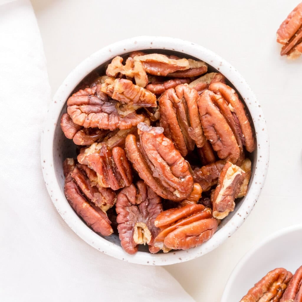 white bowl filled with maple roasted pecans on a white background.