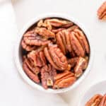 white bowl filled with maple roasted pecans on a white background.