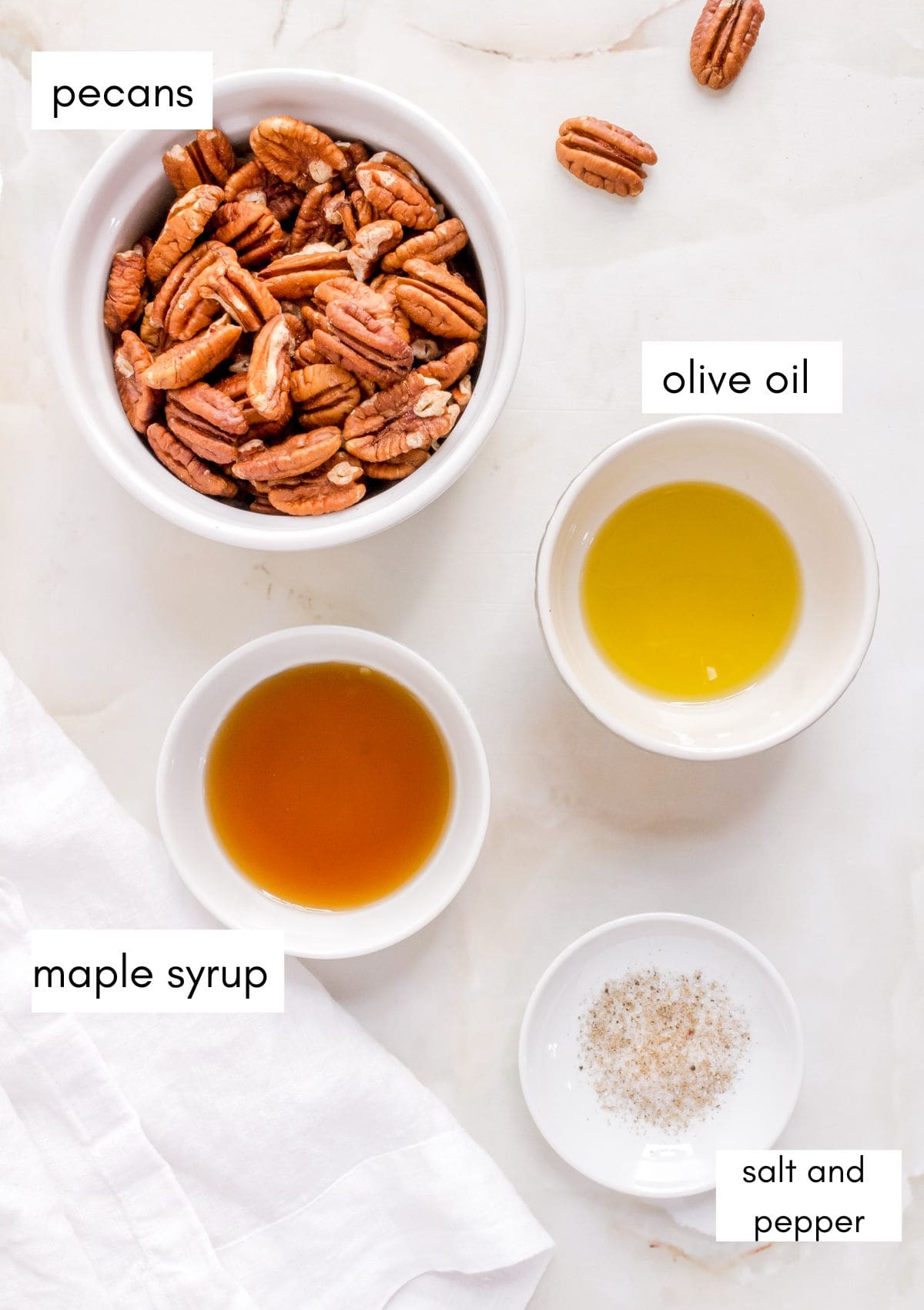 small bowls of ingredients for maple roasted pecans labeled on marble background.