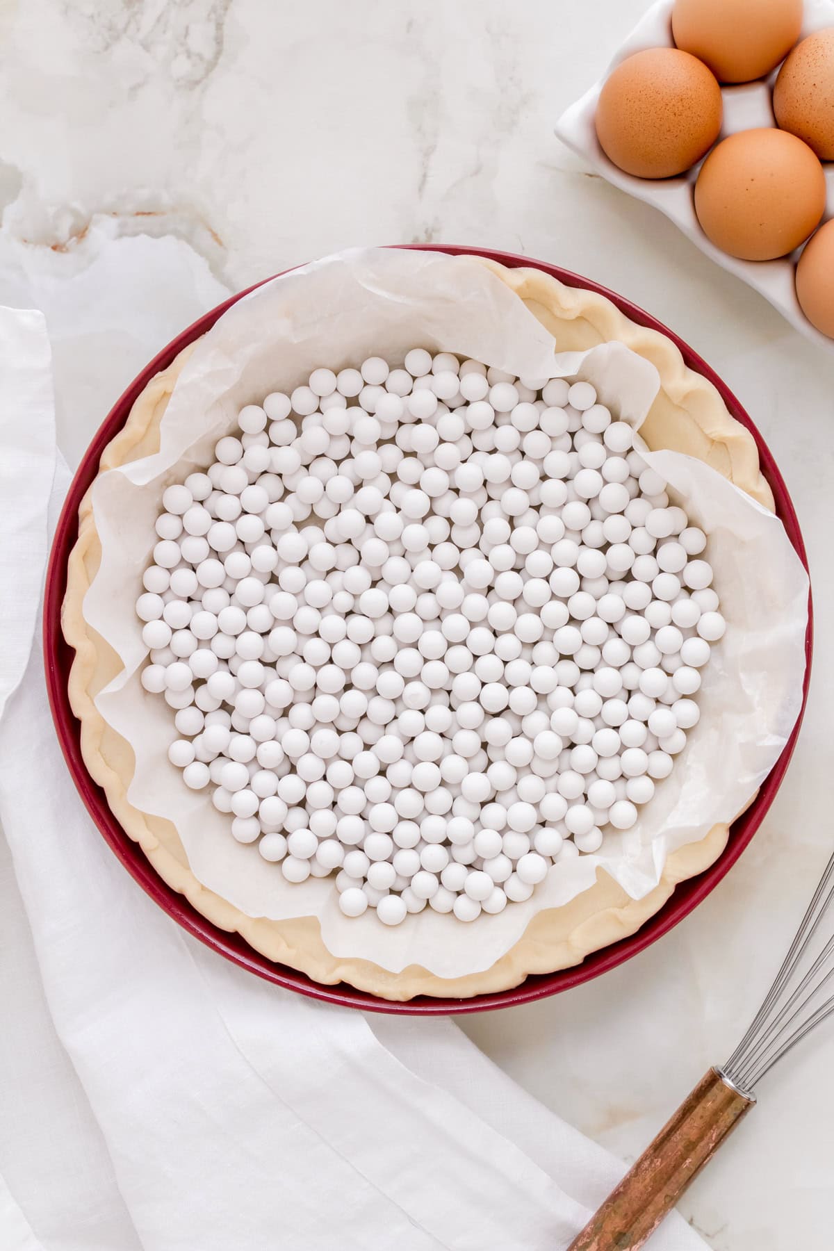 pie crust in red pie dish with parchment paper and pie weights.