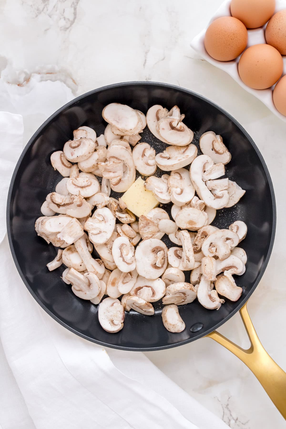 sliced white mushroom with butter in a frying pan on marble counter.