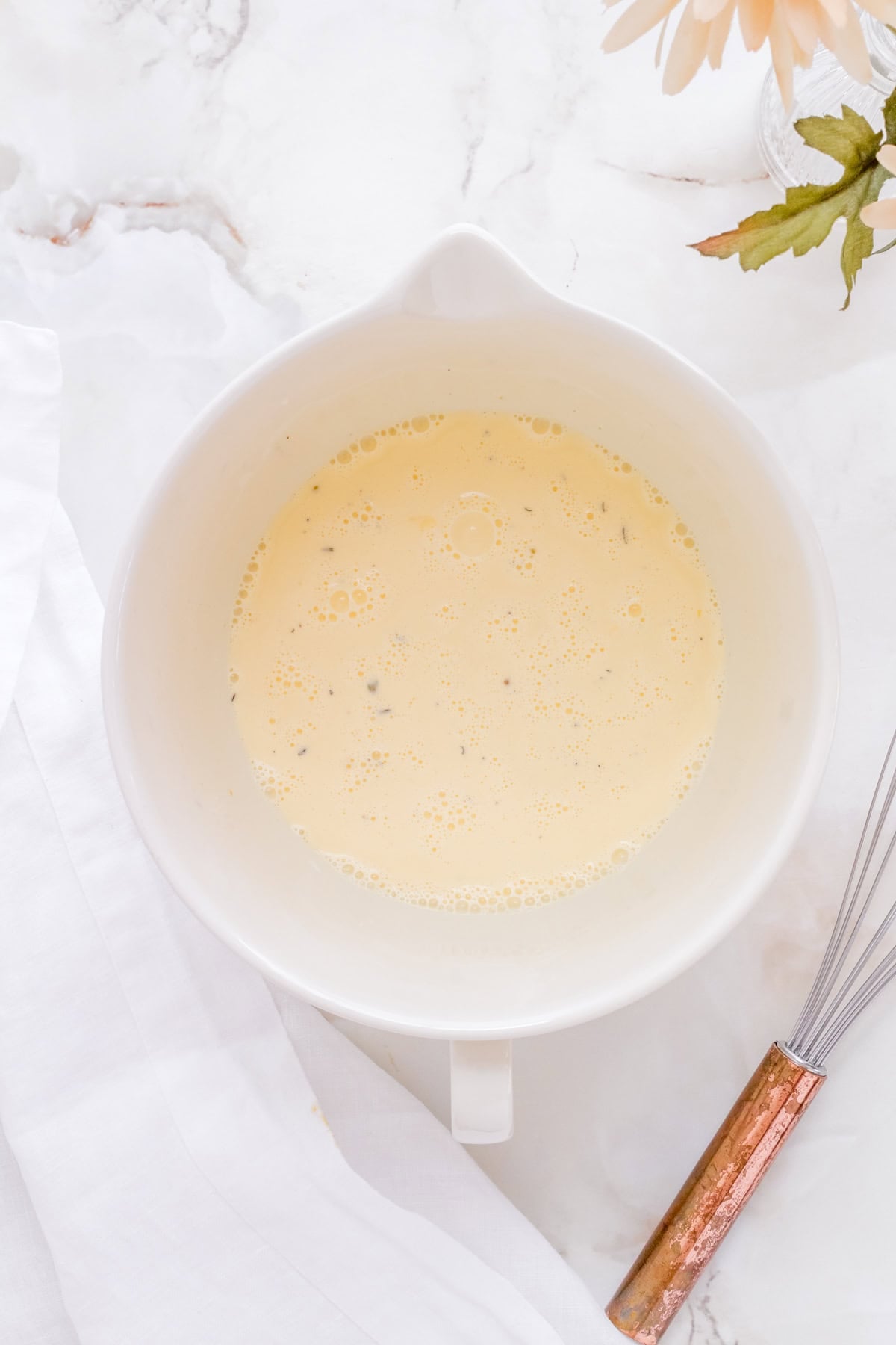 custard for quiche in a white mixing bowl with a whisk.