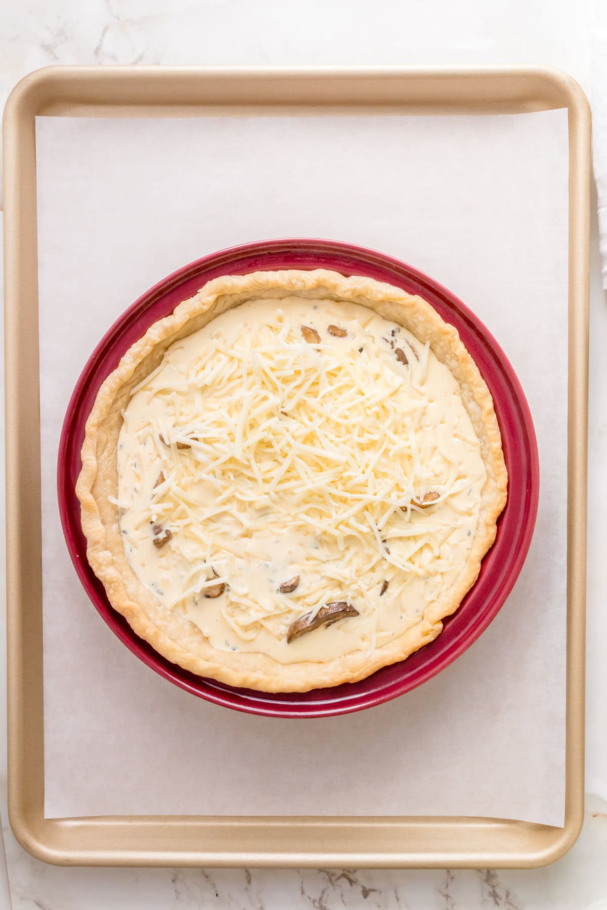 quiche in red pie dish on parchment lined baking pan.