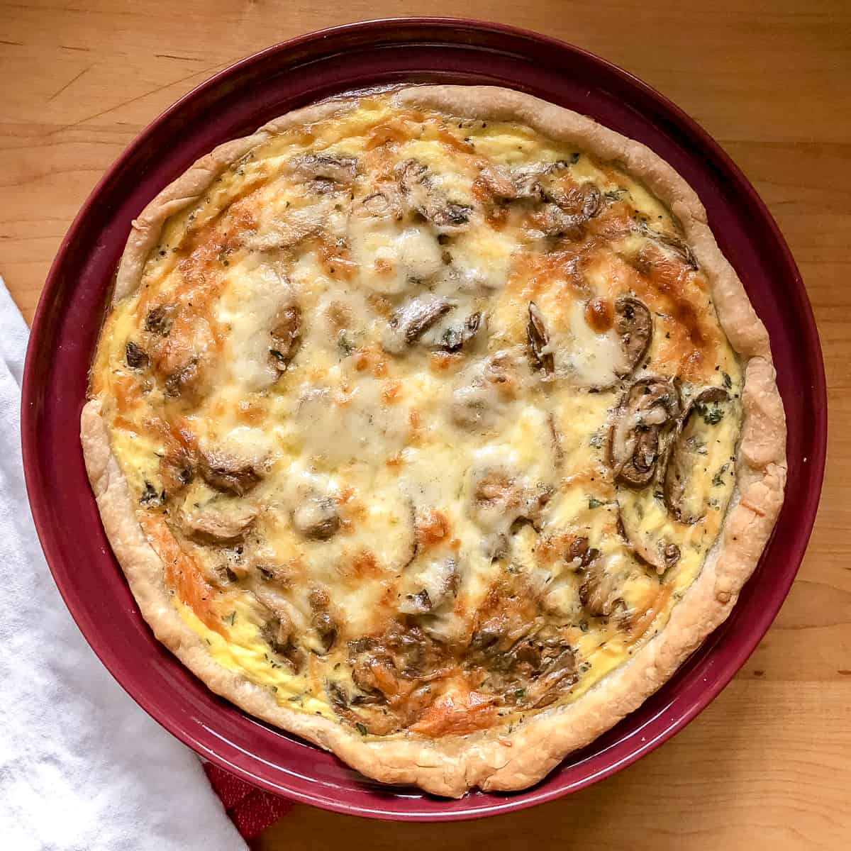 mushroom gruyere quiche in red pie pan.