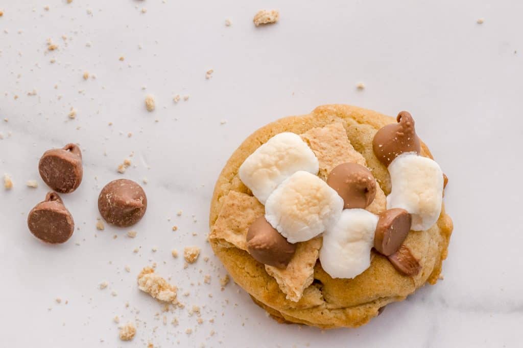 s'mores cookie on marble background with chocolate chips and graham cracker crumbs.