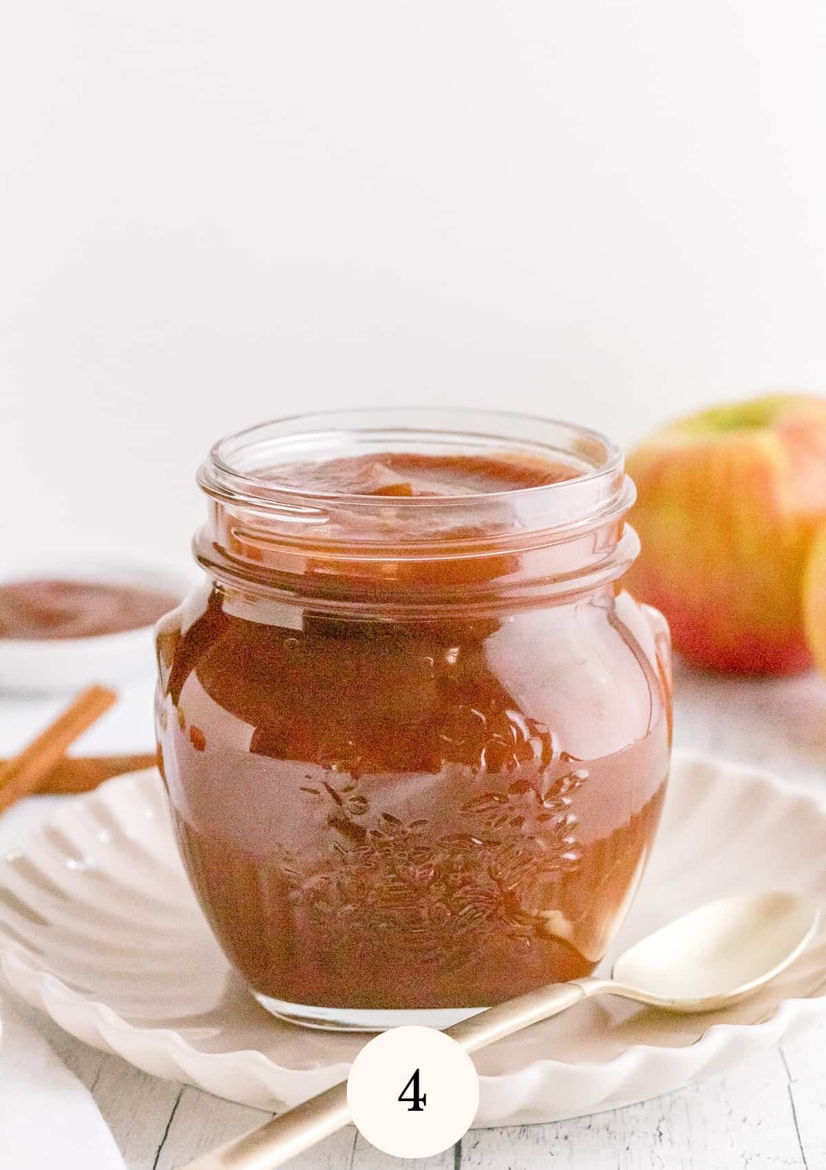 jar of slow cooker maple apple butter with apples and cinnamon sticks.