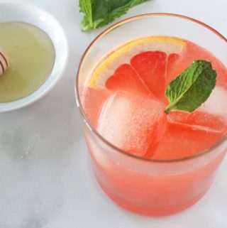 Sparkling Ruby Red Grapefruit Cocktail next to a bowl of honey