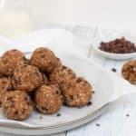 almond butter cacao energy bites on gray plate with bowl of cacao nibs