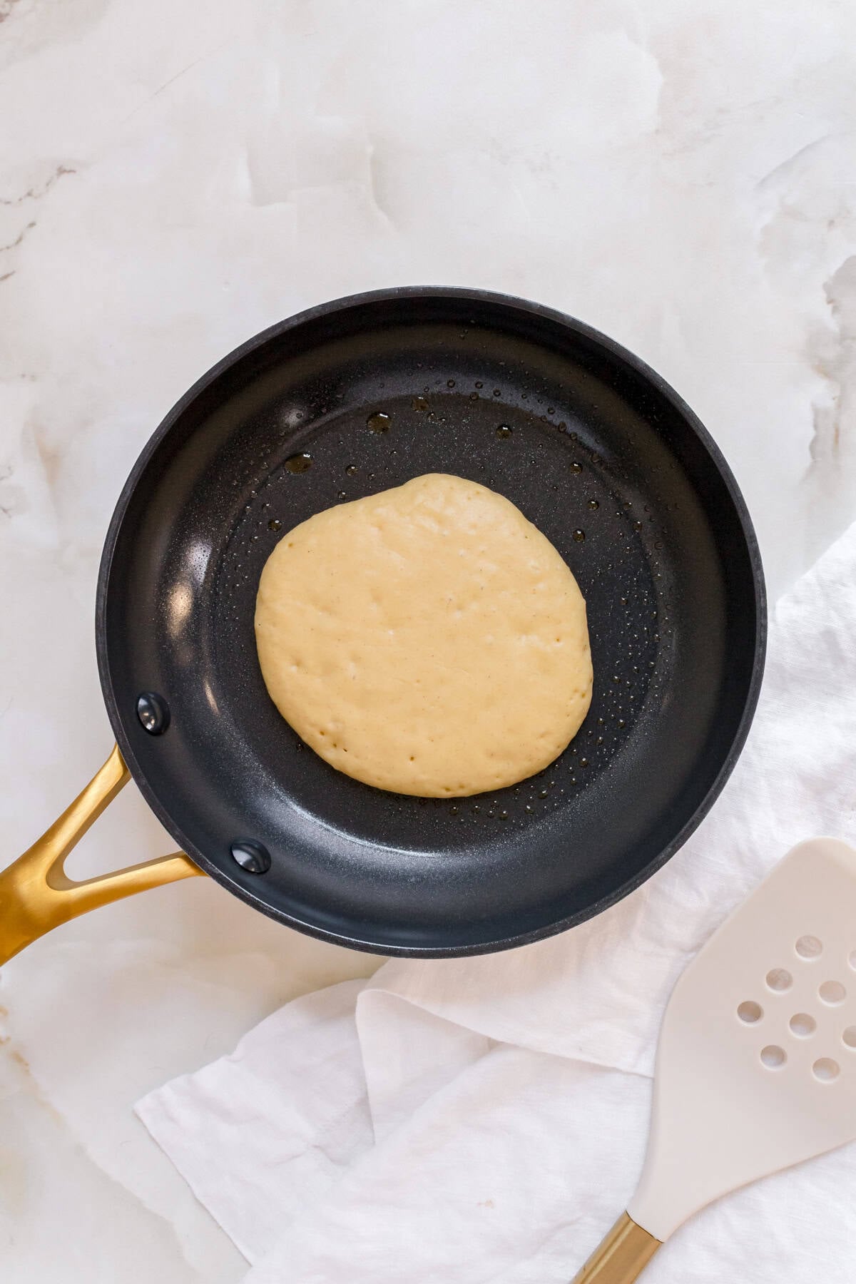gluten free pancake in a small frying pan with gold handle.