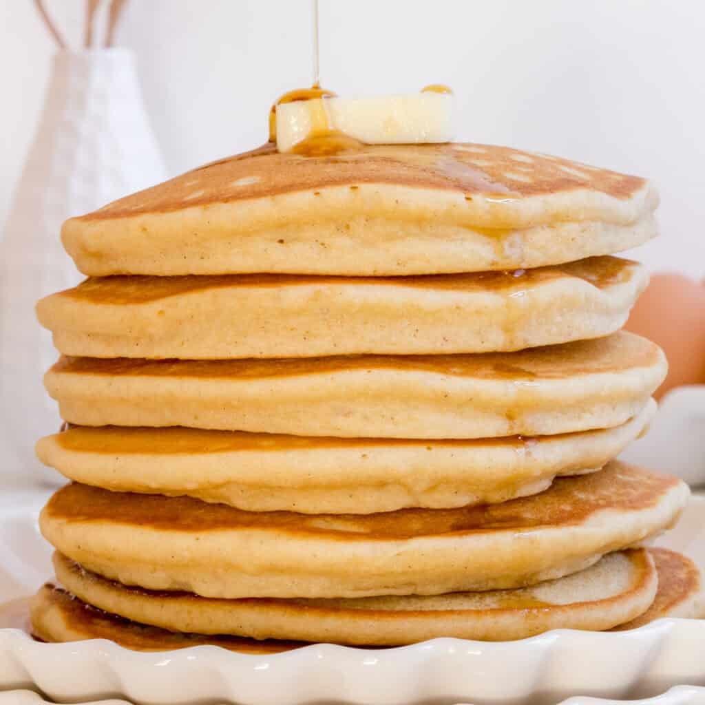 stack of gluten free pancakes on white plate with maple syrup.