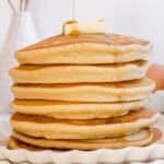 stack of gluten free pancakes on white plate with maple syrup.