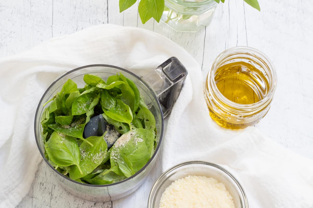 pesto ingredients in food processor with parmesan and olive oil