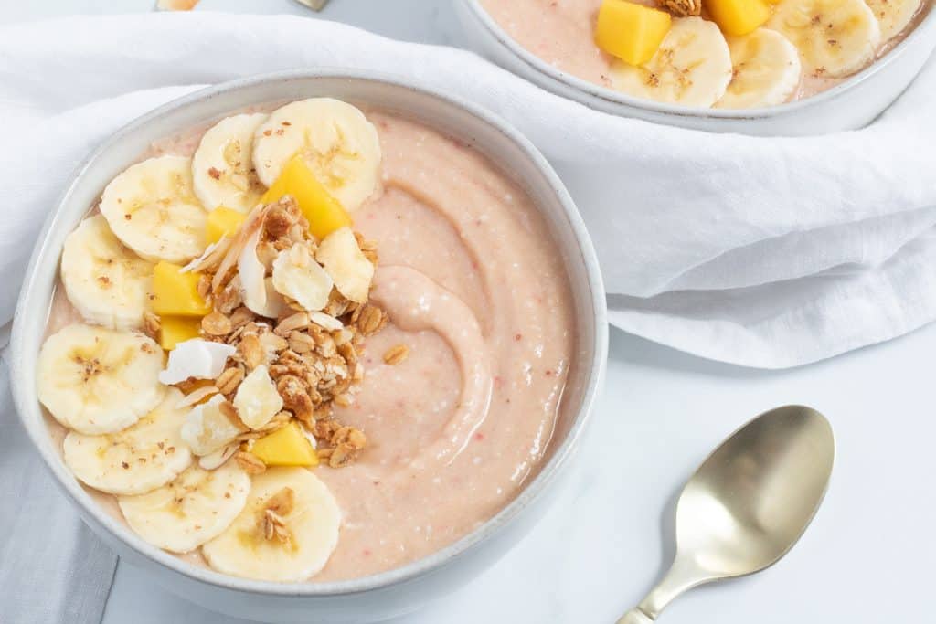 tropical smoothie bowl with spoon on white marble