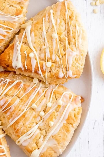 a white plate of lemon scones arranged in a circle with slices of fresh lemon and a spoon.