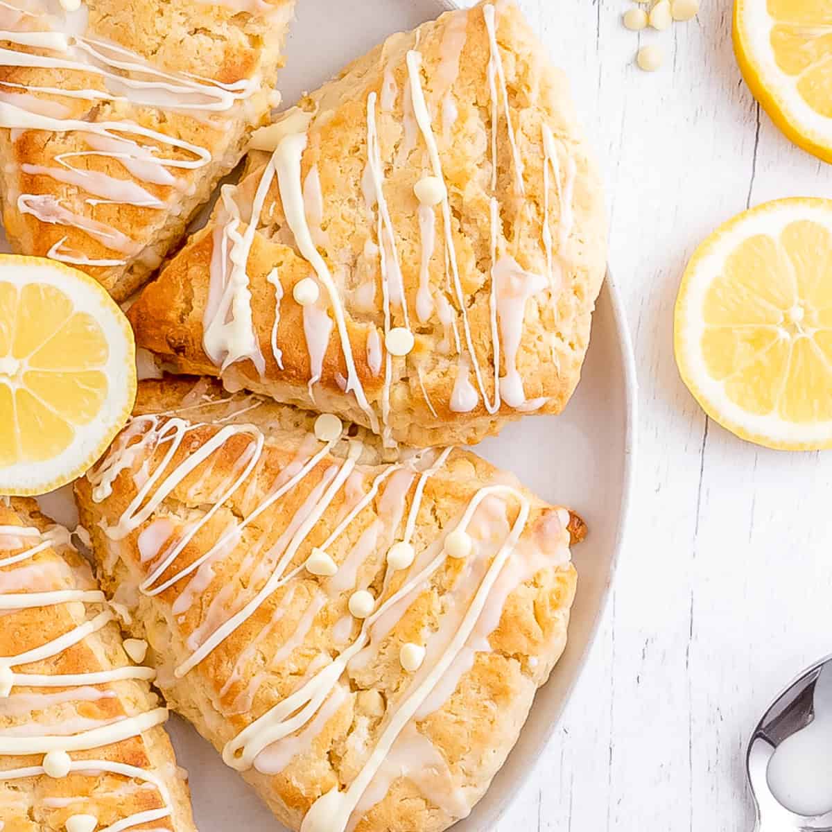 a white plate of lemon scones arranged in a circle with slices of fresh lemon and a spoon.
