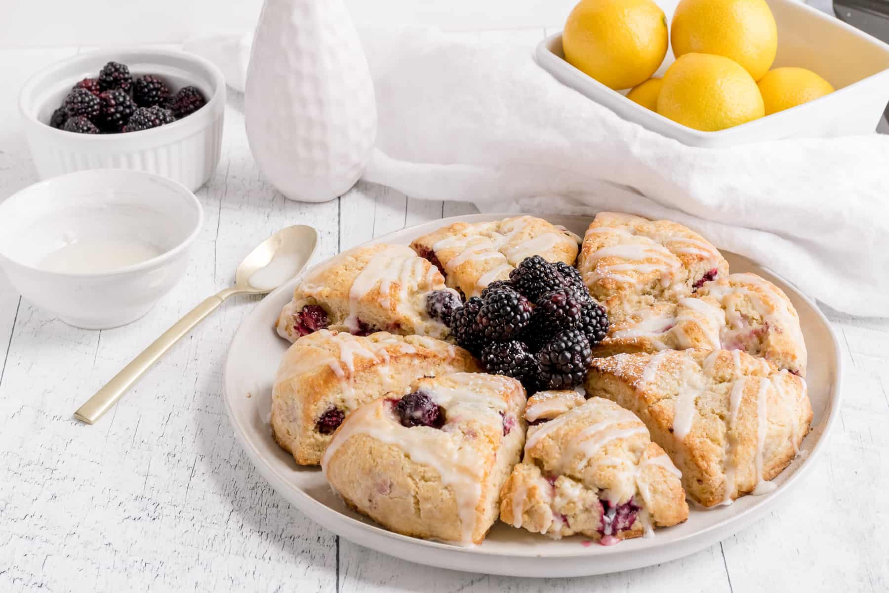 gluten free blackberry scones on plate with lemons, berries and glaze