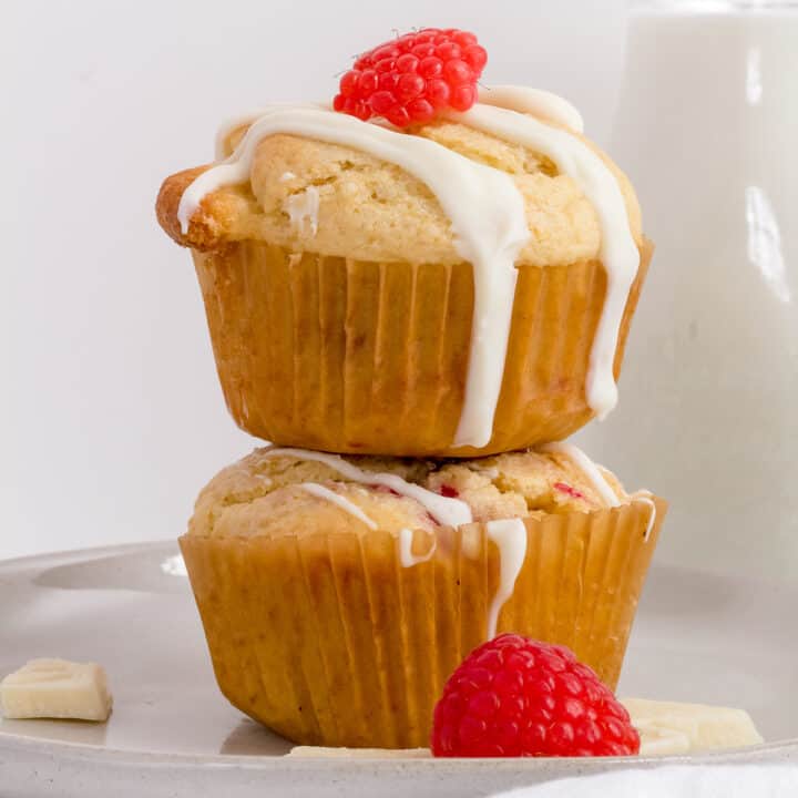 stack of raspberry white chocolate muffins on white plate with flowers and milk