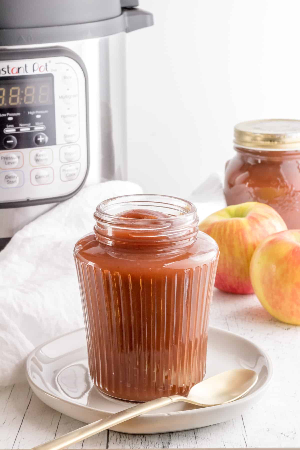 jar of apple butter with instant pot and apples.