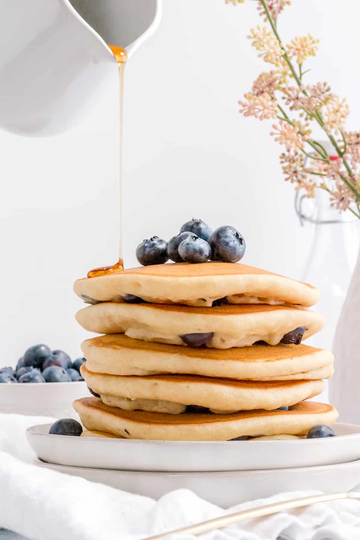 maple syrup pouring over stack of gluten free blueberry pancakes