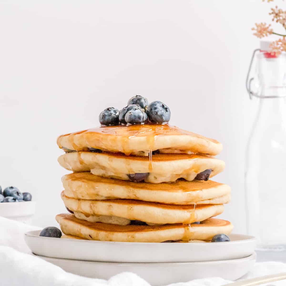 gluten free blueberry pancakes on white plate with maple syrup and blueberries.