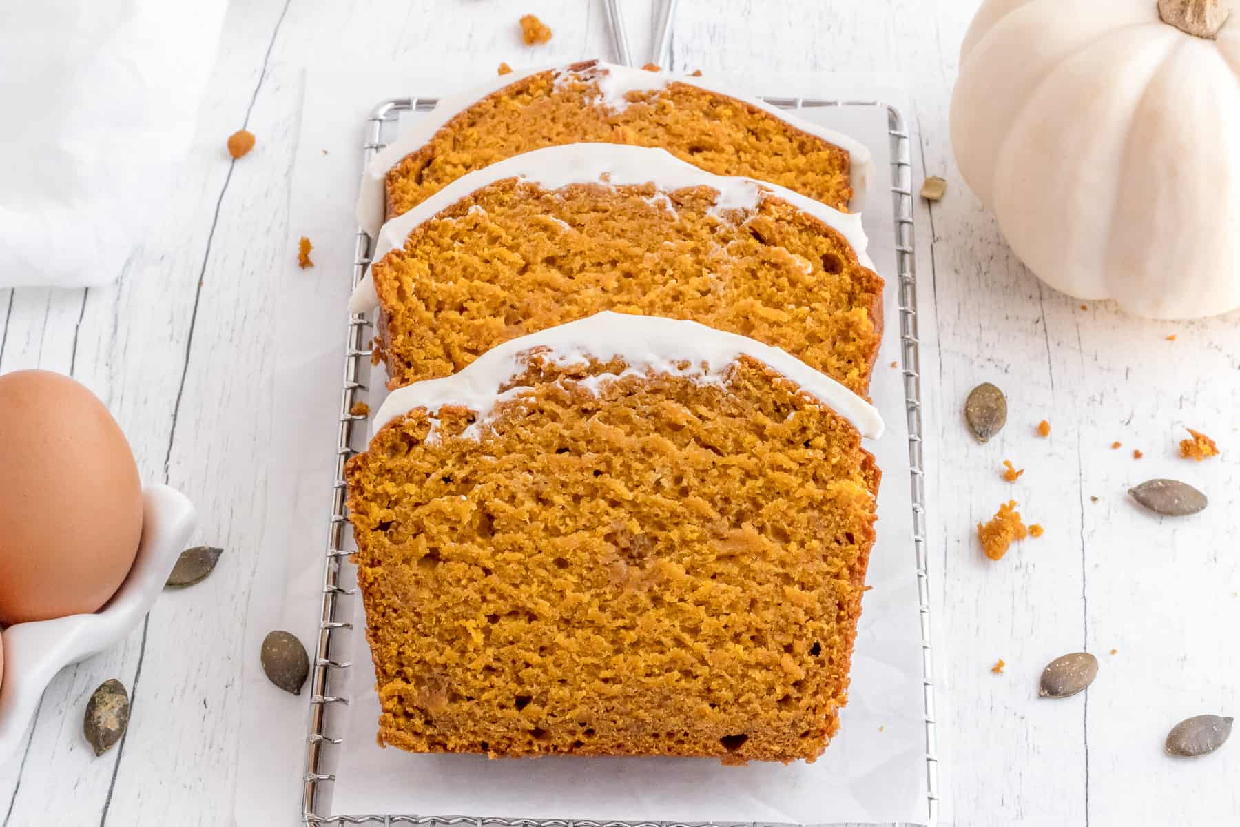 sliced loaf of pumpkin bread with cream cheese frosting on cooling rack.