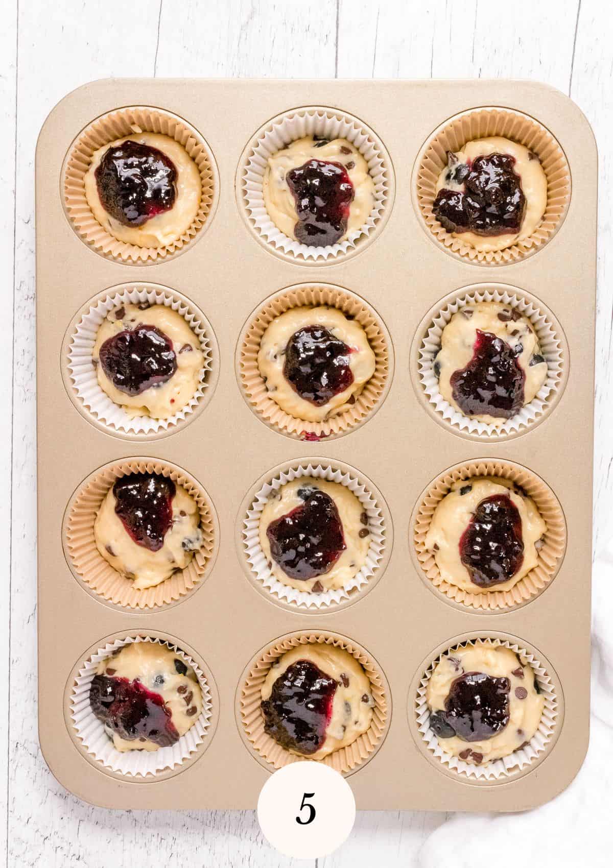 muffin batter in muffin tin with a dollop of blueberry jam.