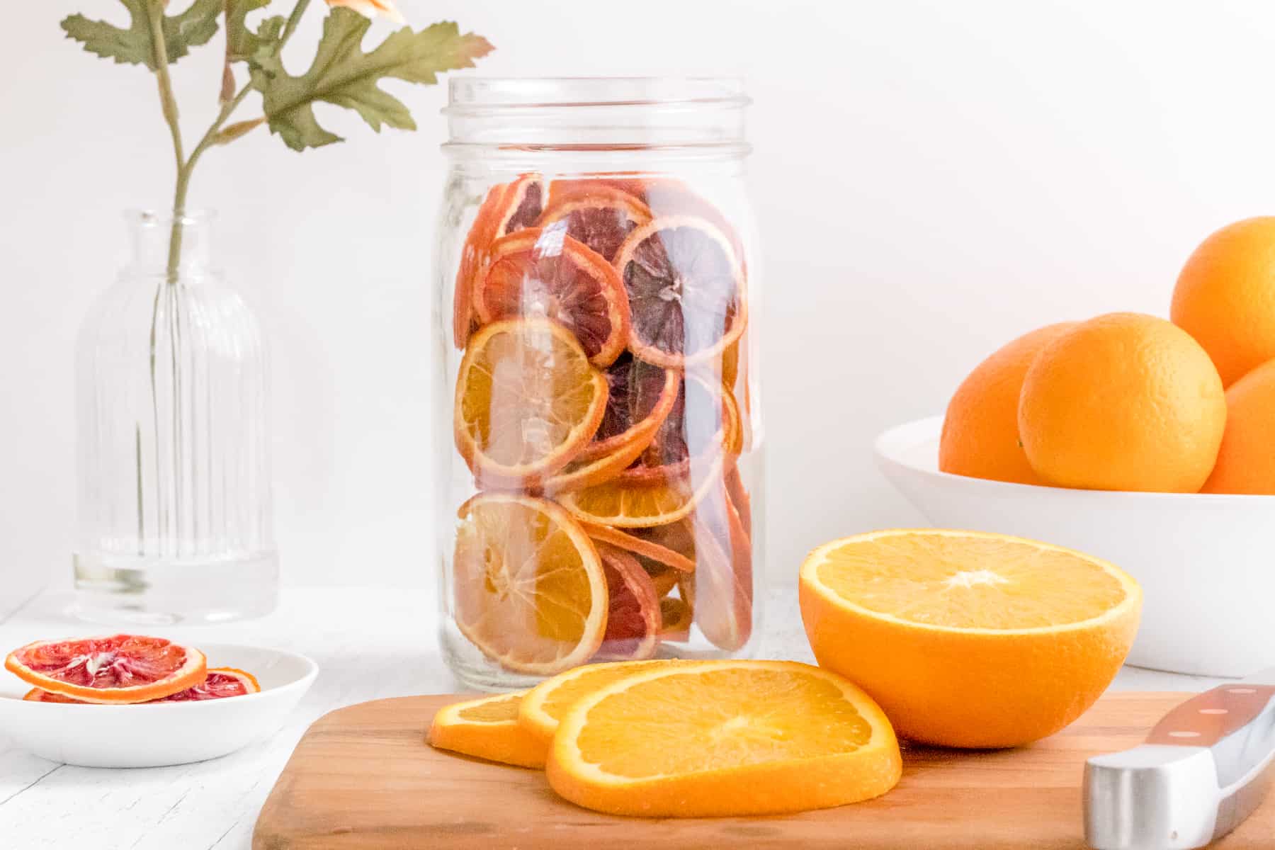 jar of dehydrated orange slices with sliced oranges  on cutting board.