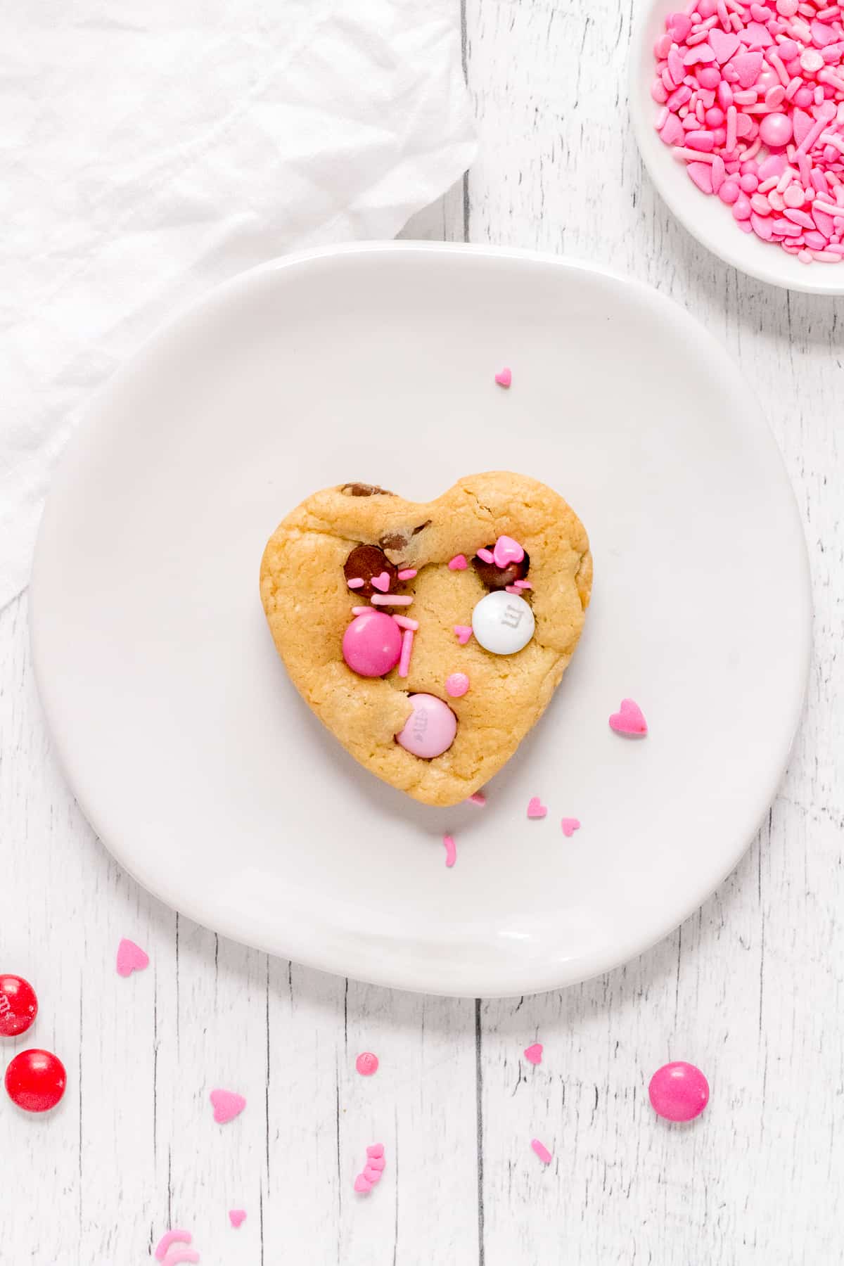 heart shaped chocolate chip cookie on a white plate with sprinkles.