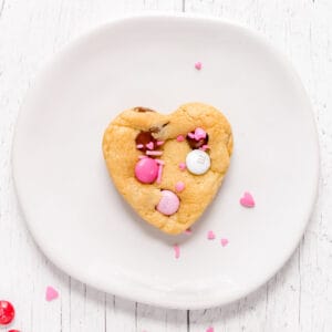 heart shaped chocolate chip cookie on white plate with sprinkles.