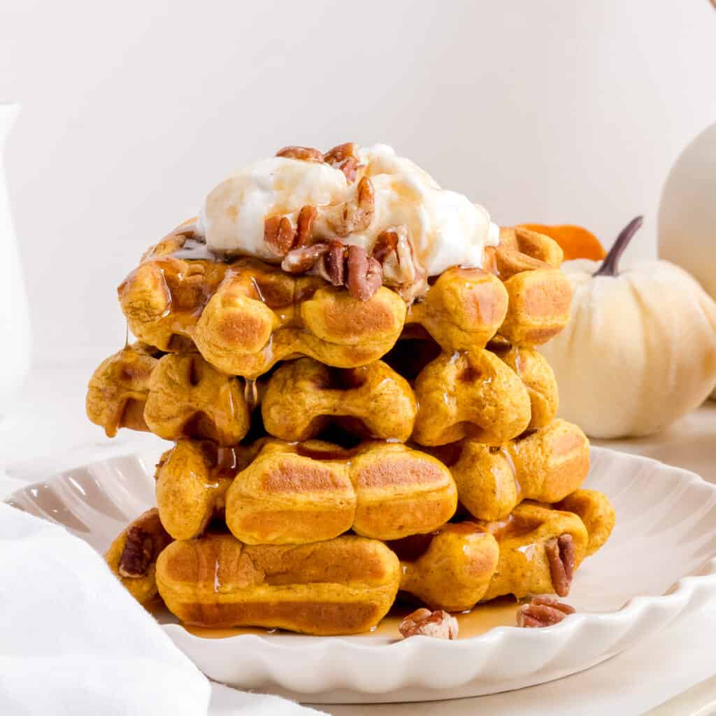 stack of pumpkin pecan waffles with whipped cream.
