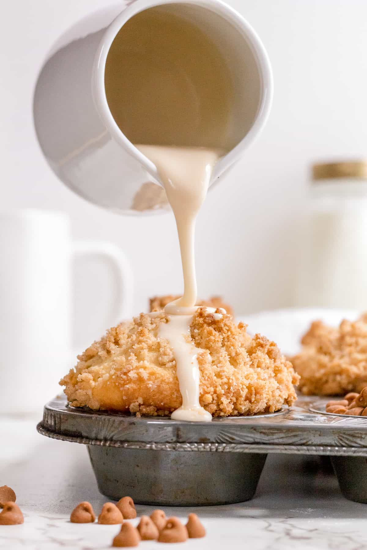 drizzling vanilla glaze over cinnamon streusel muffins in pan.