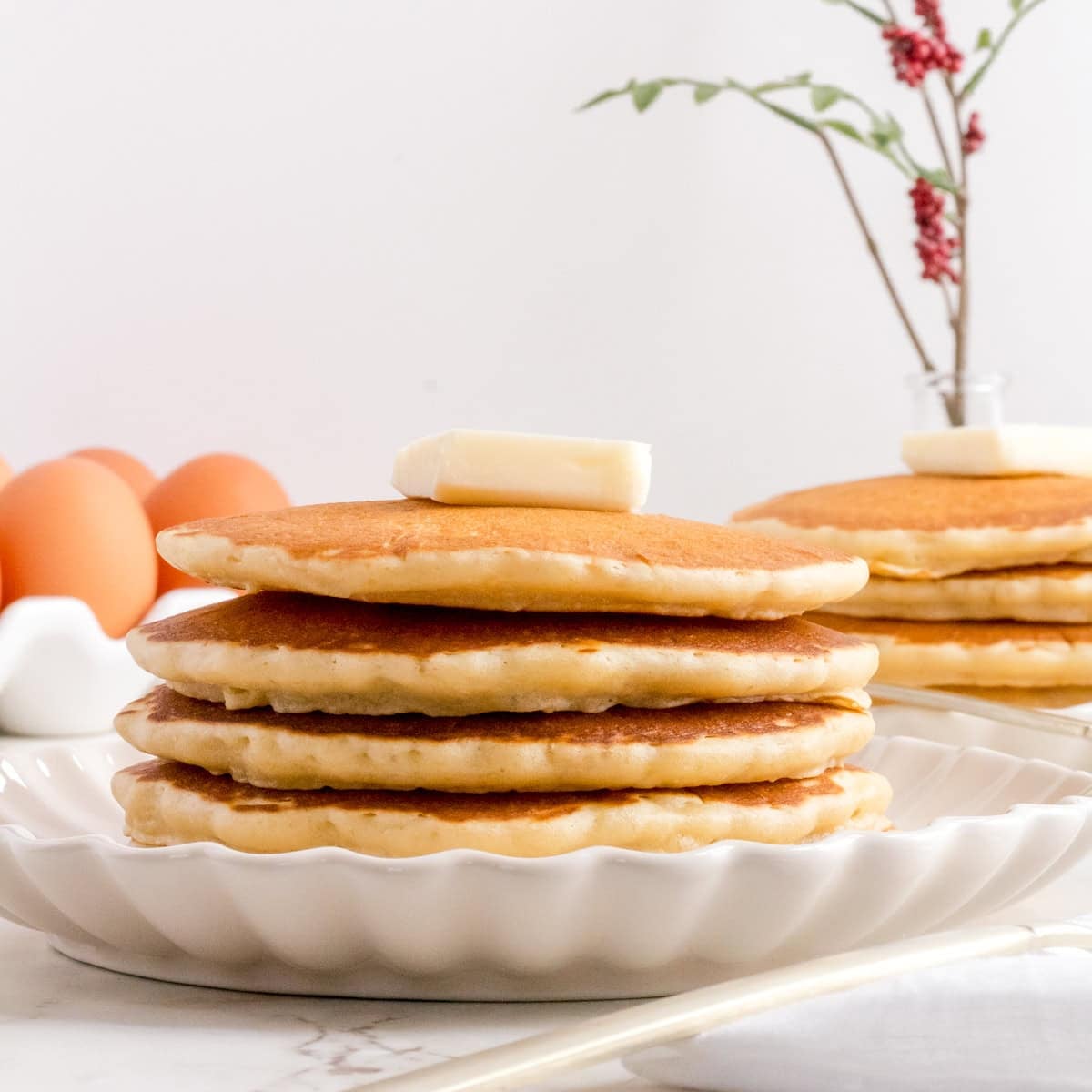 stack of pancakes for two on white plate with butter.