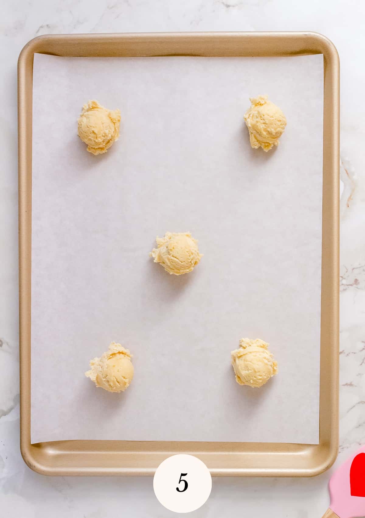 balls of almond sugar cookie dough on parchment lined sheet pan.