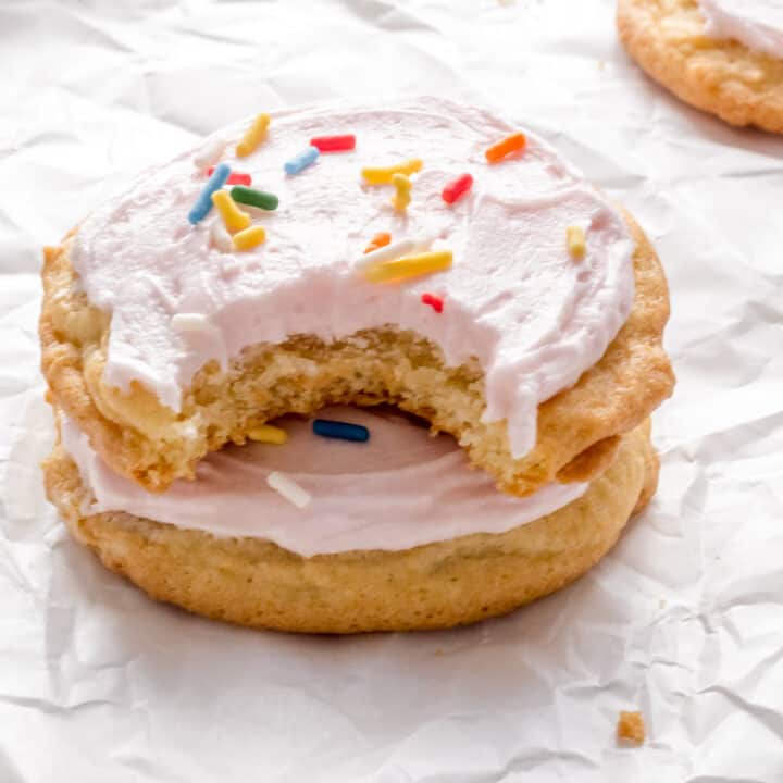 stack of soft almond sugar cookies with pink buttercream and sprinkles.