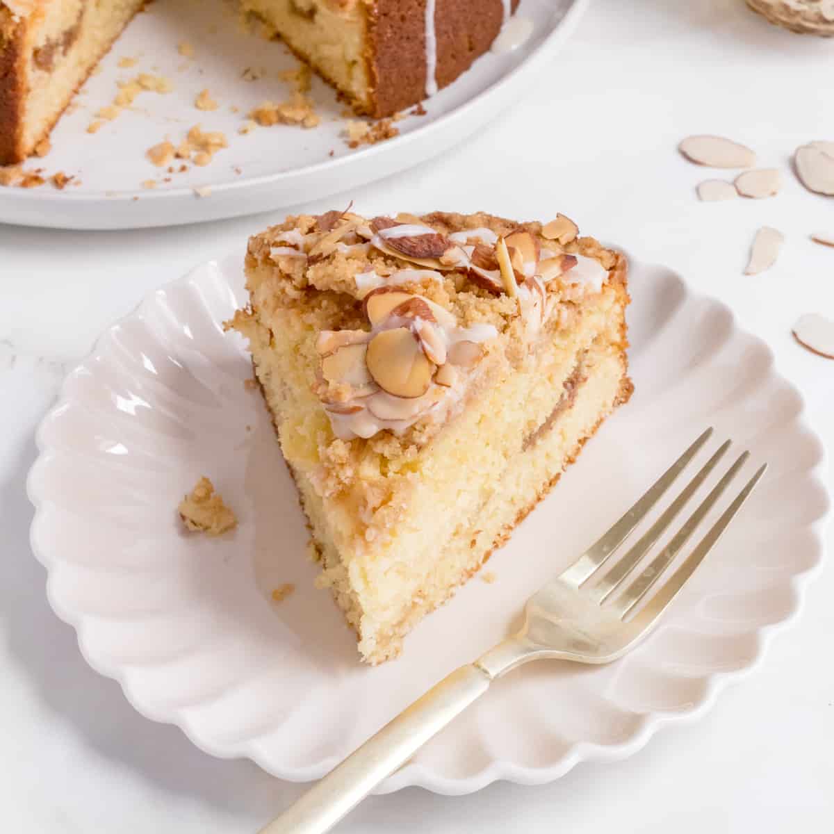 slice of almond coffee cake with almond glaze on white plate.