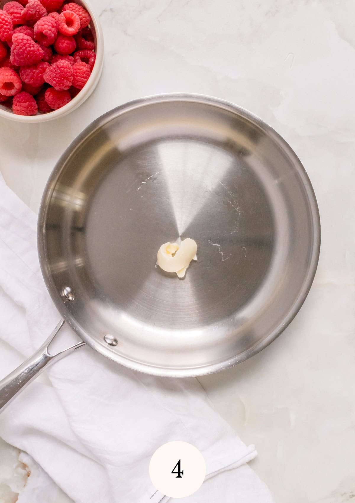 A small piece of butter melts in a stainless steel frying pan.