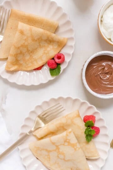 gluten free crepes on plates with a bowl of nutella and whipped cream.
