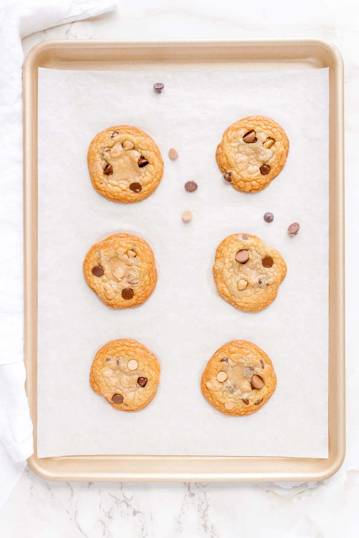 baked cookies on a sheet pan adding extra peanut butter chips.