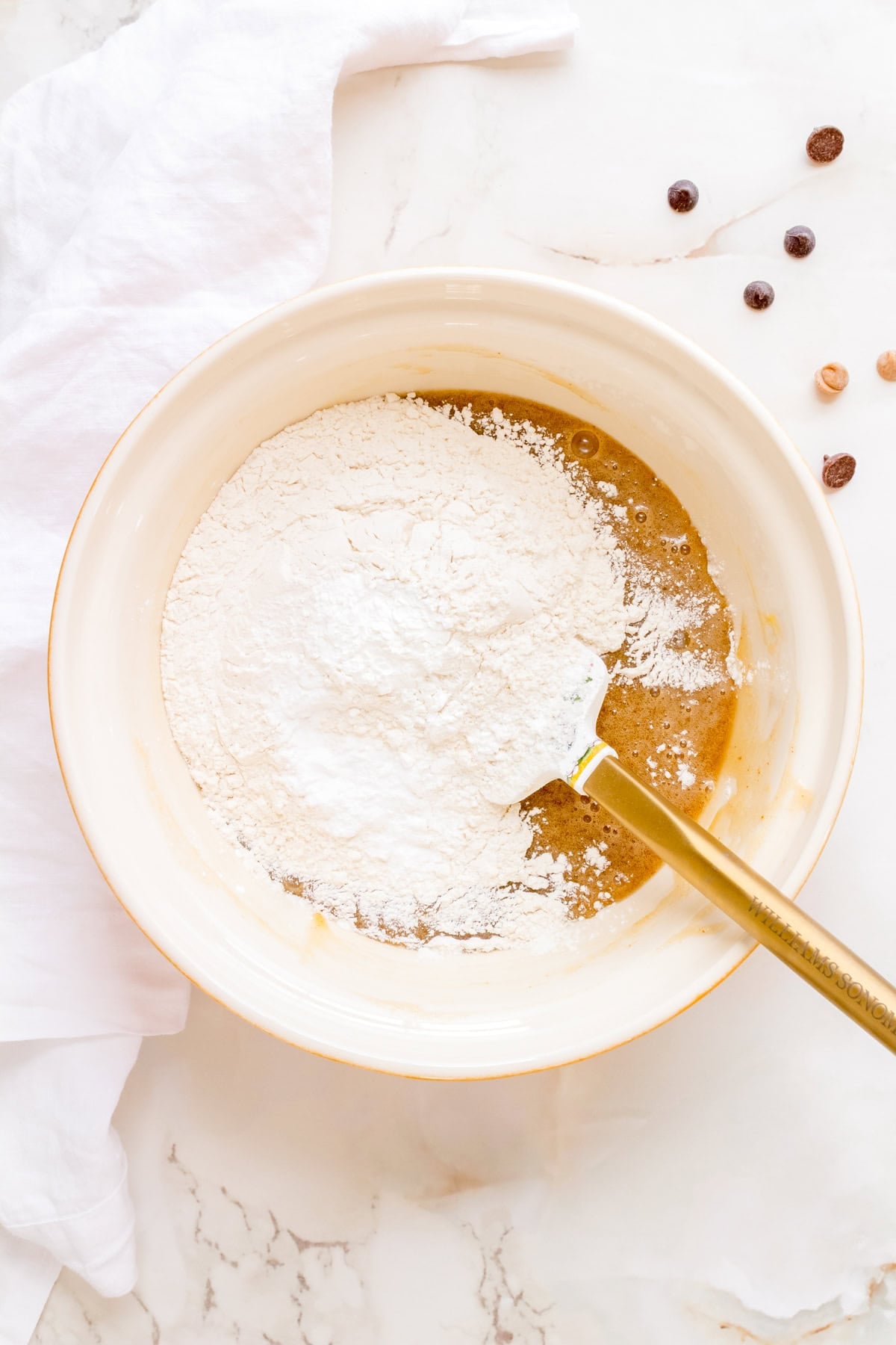 dry ingredients added to cookie dough in ceramic mixing bowl.