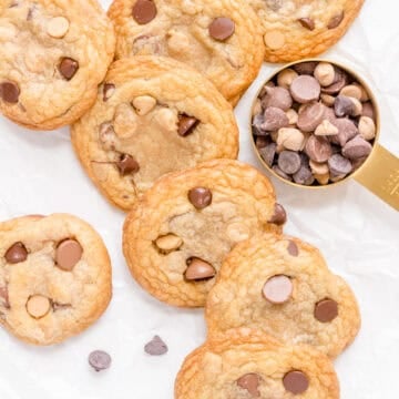 chocolate chip and peanut butter chip cookies in a stack with a gold cup of peanut butter chips and chocolate chips.