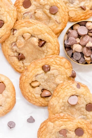 chocolate chip and peanut butter chip cookies in a stack with a gold cup of peanut butter chips and chocolate chips.