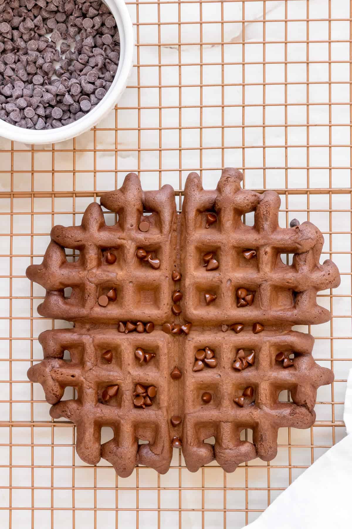 chocolate waffle on metal cooling rack sprinkled with mini chocolate chips.