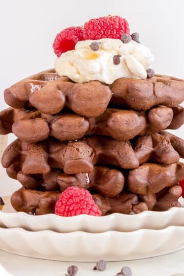 a stack of triple chocolate waffles with raspberries and whipped cream.