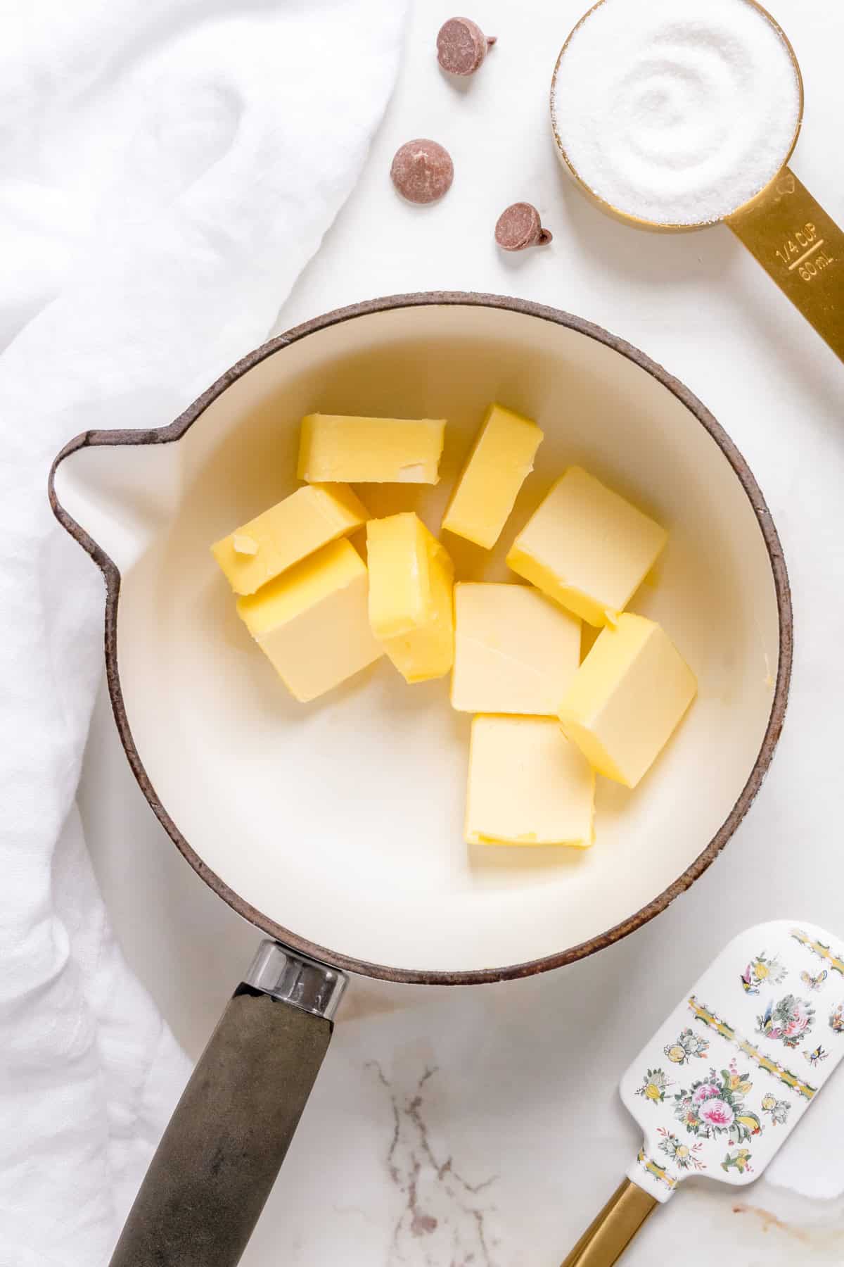 pieces of unsalted butter in white saucepan with black handle.