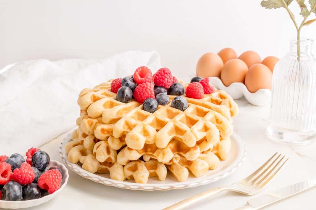 a stack of buttermilk waffles on a white plate with fresh blueberries and raspberries. 