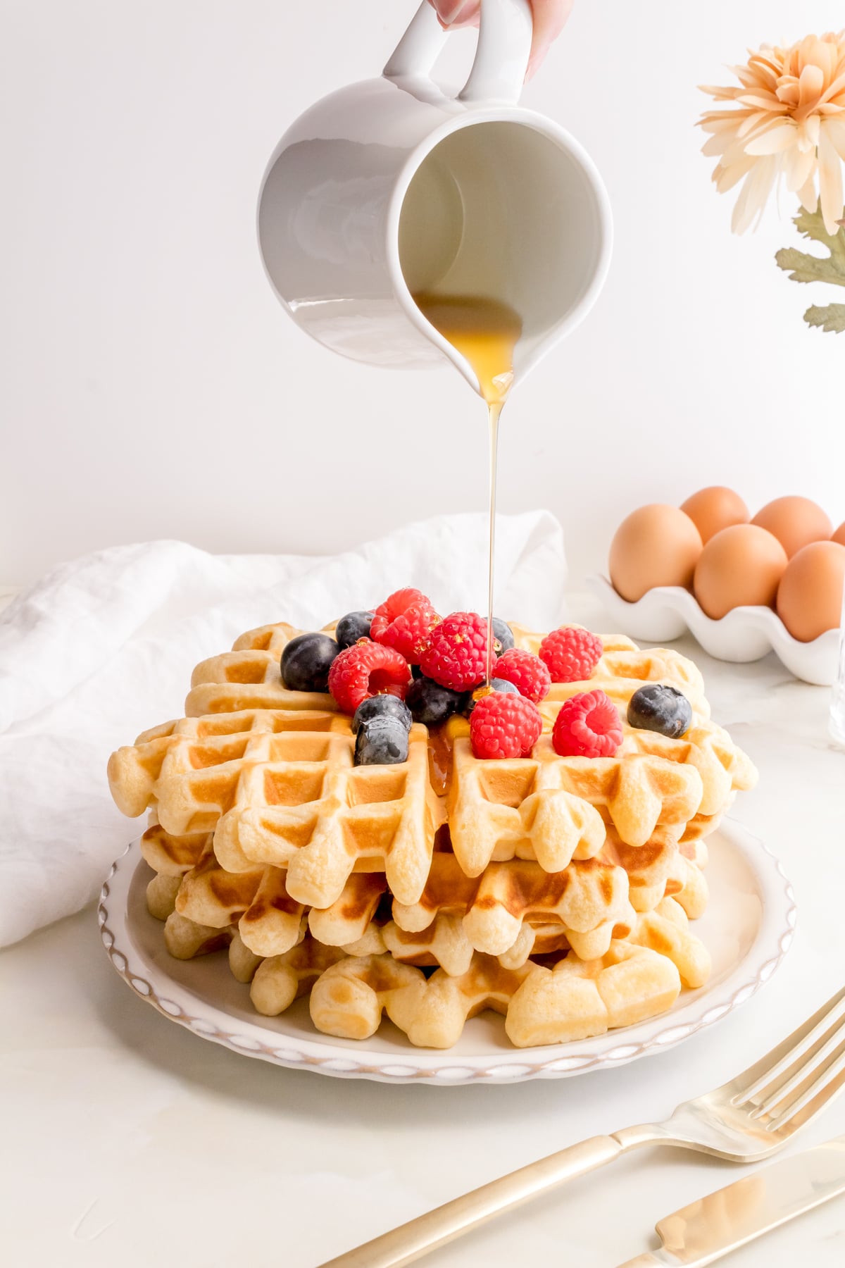 maple syrup pouring over buttermilk waffles with berries.